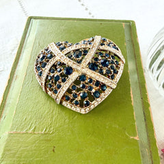 Vintage heart brooch with Montana sapphire and clear rhinestones in silver‑tone metal with gold wash, displayed on lace with a green book and pink flower