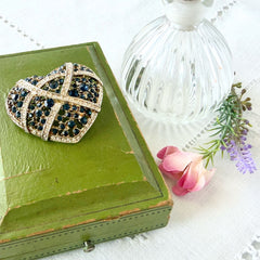 Vintage heart brooch with Montana sapphire and clear rhinestones in silver‑tone metal with gold wash, displayed on lace with a green book and pink flower