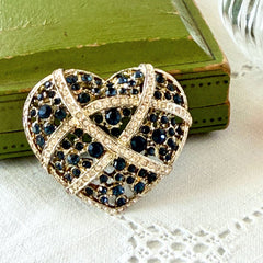 Vintage heart brooch with Montana sapphire and clear rhinestones in silver‑tone metal with gold wash, displayed on lace with a green book and pink flower