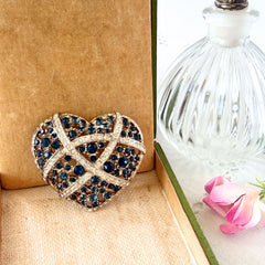 Vintage heart brooch with Montana sapphire and clear rhinestones in silver‑tone metal with gold wash, displayed on lace with a green book and pink flower