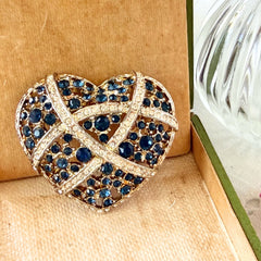 Vintage heart brooch with Montana sapphire and clear rhinestones in silver‑tone metal with gold wash, displayed on lace with a green book and pink flower