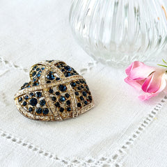 Vintage heart brooch with Montana sapphire and clear rhinestones in silver‑tone metal with gold wash, displayed on lace with a green book and pink flower
