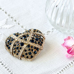 Vintage heart brooch with Montana sapphire and clear rhinestones in silver‑tone metal with gold wash, displayed on lace with a green book and pink flower