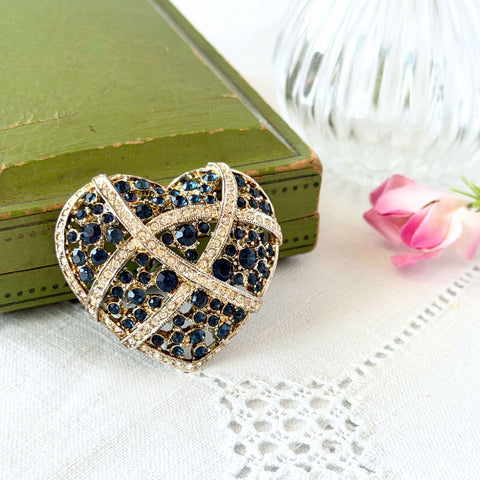 Vintage heart brooch with Montana sapphire and clear rhinestones in silver‑tone metal with gold wash, displayed on lace with a green book and pink flower