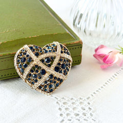 Vintage heart brooch with Montana sapphire and clear rhinestones in silver‑tone metal with gold wash, displayed on lace with a green book and pink flower
