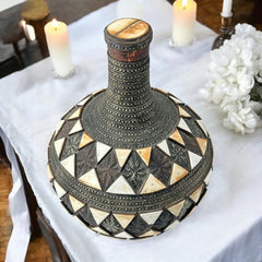 Vintage Moroccan pottery vase from the 1970s/80s, featuring a large clay body with ornate metal inlays, an antiqued bronze/brass finish, and three geometric rings of camel bone triangle patterns. Includes an original metal lid, reflecting its historic use for storing and transporting liquids. In very good vintage condition, showcasing intricate craftsmanship and cultural heritage.
