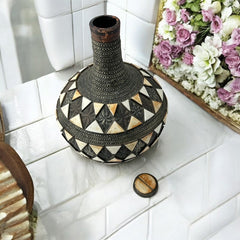 Vintage Moroccan pottery vase from the 1970s/80s, featuring a large clay body with ornate metal inlays, an antiqued bronze/brass finish, and three geometric rings of camel bone triangle patterns. Includes an original metal lid, reflecting its historic use for storing and transporting liquids. In very good vintage condition, showcasing intricate craftsmanship and cultural heritage.