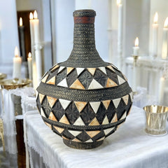 Vintage Moroccan pottery vase from the 1970s/80s, featuring a large clay body with ornate metal inlays, an antiqued bronze/brass finish, and three geometric rings of camel bone triangle patterns. Includes an original metal lid, reflecting its historic use for storing and transporting liquids. In very good vintage condition, showcasing intricate craftsmanship and cultural heritage.