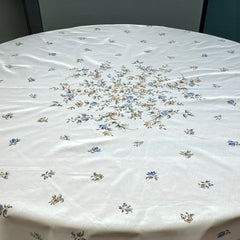 Round coated cotton tablecloth in white with polychrome and blue Provençal motifs, featuring birds, butterflies, and floral designs inspired by traditional Moustiers faience