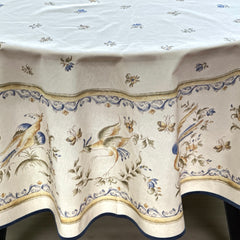 Round coated cotton tablecloth in white with polychrome and blue Provençal motifs, featuring birds, butterflies, and floral designs inspired by traditional Moustiers faience
