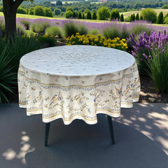 Round coated cotton tablecloth in white with polychrome and blue Provençal motifs, featuring birds, butterflies, and floral designs inspired by traditional Moustiers faience