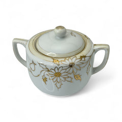Vintage Nippon porcelain sugar bowl and creamer set with hand-painted gold floral design on white glaze; sugar bowl with dual handles and lid, creamer with spout and single handle; both marked “Hand Painted Nippon” with sun emblem on base.