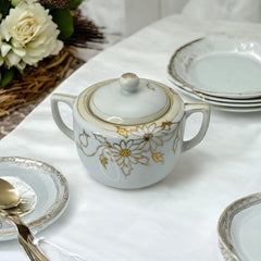 Vintage Nippon porcelain sugar bowl and creamer set with hand-painted gold floral design on white glaze; sugar bowl with dual handles and lid, creamer with spout and single handle; both marked “Hand Painted Nippon” with sun emblem on base.