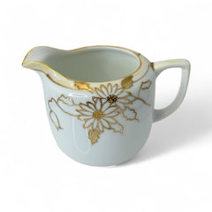 Vintage Nippon porcelain sugar bowl and creamer set with hand-painted gold floral design on white glaze; sugar bowl with dual handles and lid, creamer with spout and single handle; both marked “Hand Painted Nippon” with sun emblem on base.