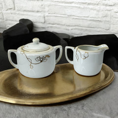 Vintage Nippon porcelain sugar bowl and creamer set with hand-painted gold floral design on white glaze; sugar bowl with dual handles and lid, creamer with spout and single handle; both marked “Hand Painted Nippon” with sun emblem on base.