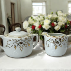Vintage Nippon porcelain sugar bowl and creamer set with hand-painted gold floral design on white glaze; sugar bowl with dual handles and lid, creamer with spout and single handle; both marked “Hand Painted Nippon” with sun emblem on base.
