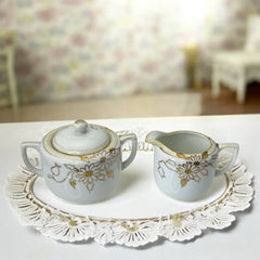 Vintage Nippon porcelain sugar bowl and creamer set with hand-painted gold floral design on white glaze; sugar bowl with dual handles and lid, creamer with spout and single handle; both marked “Hand Painted Nippon” with sun emblem on base.