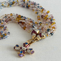 Vintage Nolan Miller necklace with an ornate enamel and rhinestone cross pendant on an eight‑strand pastel faceted glass bead torsade in gold‑tone metal.