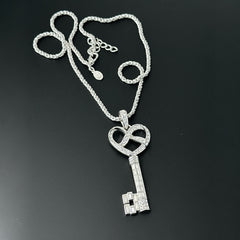 Vintage Nolan Miller silver-tone key pendant necklace with clear rhinestones in heart and infinity design, shown on twisted rope chain.