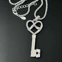 Vintage Nolan Miller silver-tone key pendant necklace with clear rhinestones in heart and infinity design, shown on twisted rope chain.