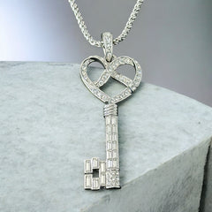 Vintage Nolan Miller silver-tone key pendant necklace with clear rhinestones in heart and infinity design, shown on twisted rope chain.