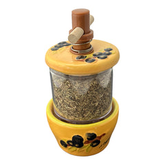 Provence hand-painted ceramic herb grinder with a yellow base featuring black olive and green leaf design, filled with dried Herbes de Provence. 