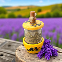 Provence hand-painted ceramic herb grinder with a yellow base featuring black olive and green leaf design, filled with dried Herbes de Provence. 