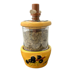 Provence hand-painted ceramic herb grinder with a yellow base featuring black olive and green leaf design, filled with dried Herbes de Provence. 