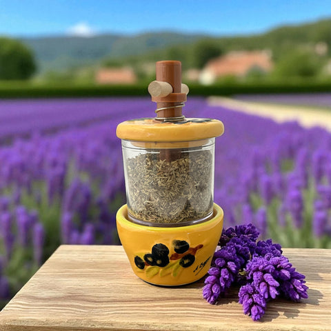 Provence hand-painted ceramic herb grinder with a yellow base featuring black olive and green leaf design, filled with dried Herbes de Provence. 