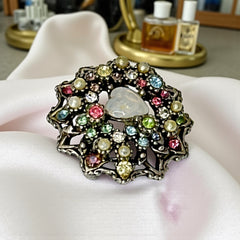 Vintage silver tone brooch with ornate round filigree design, featuring a central opalite heart cabochon and pastel rhinestones in pink, blue, yellow, and lavender—shown front and back to highlight detailing and clasp.