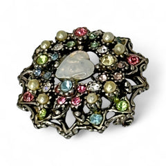 Vintage silver tone brooch with ornate round filigree design, featuring a central opalite heart cabochon and pastel rhinestones in pink, blue, yellow, and lavender—shown front and back to highlight detailing and clasp.