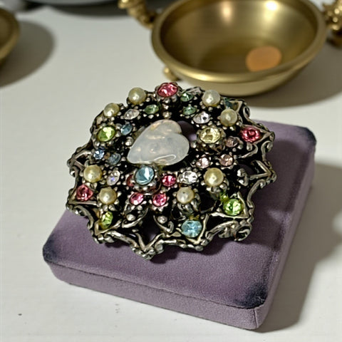 Vintage silver tone brooch with ornate round filigree design, featuring a central opalite heart cabochon and pastel rhinestones in pink, blue, yellow, and lavender—shown front and back to highlight detailing and clasp.
