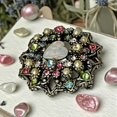 Vintage silver tone brooch with ornate round filigree design, featuring a central opalite heart cabochon and pastel rhinestones in pink, blue, yellow, and lavender—shown front and back to highlight detailing and clasp.