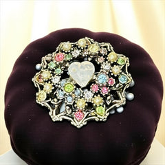 Vintage silver tone brooch with ornate round filigree design, featuring a central opalite heart cabochon and pastel rhinestones in pink, blue, yellow, and lavender—shown front and back to highlight detailing and clasp.