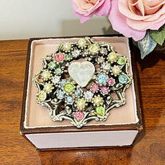 Vintage silver tone brooch with ornate round filigree design, featuring a central opalite heart cabochon and pastel rhinestones in pink, blue, yellow, and lavender—shown front and back to highlight detailing and clasp.