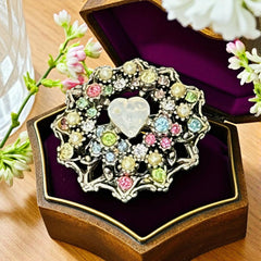 Vintage silver tone brooch with ornate round filigree design, featuring a central opalite heart cabochon and pastel rhinestones in pink, blue, yellow, and lavender—shown front and back to highlight detailing and clasp.