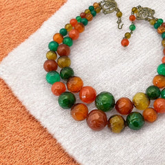 Vintage 1950s 2-strand graduated necklace featuring transparent and opaque orange and green plastic beads, finished with gold-tone findings and an adjustable hook clasp, in very good vintage condition.