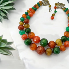 Vintage 1950s 2-strand graduated necklace featuring transparent and opaque orange and green plastic beads, finished with gold-tone findings and an adjustable hook clasp, in very good vintage condition.