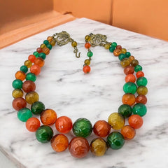 Vintage 1950s 2-strand graduated necklace featuring transparent and opaque orange and green plastic beads, finished with gold-tone findings and an adjustable hook clasp, in very good vintage condition.