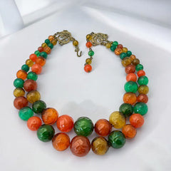Vintage 1950s 2-strand graduated necklace featuring transparent and opaque orange and green plastic beads, finished with gold-tone findings and an adjustable hook clasp, in very good vintage condition.