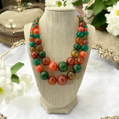 Vintage 1950s 2-strand graduated necklace featuring transparent and opaque orange and green plastic beads, finished with gold-tone findings and an adjustable hook clasp, in very good vintage condition.