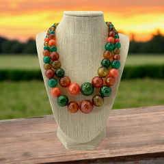 Vintage 1950s 2-strand graduated necklace featuring transparent and opaque orange and green plastic beads, finished with gold-tone findings and an adjustable hook clasp, in very good vintage condition.