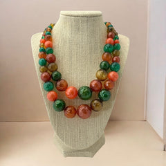 Vintage 1950s 2-strand graduated necklace featuring transparent and opaque orange and green plastic beads, finished with gold-tone findings and an adjustable hook clasp, in very good vintage condition.