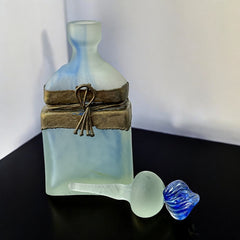 Vintage Romanian art glass perfume bottle from the 1990s, featuring frosted blue and green glass with a sculptural swirled stopper and bronze wire bow detail around the neck. Square base with a tapered neck; dauber slightly shortened due to breakage.
