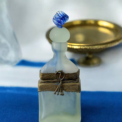 Vintage Romanian art glass perfume bottle from the 1990s, featuring frosted blue and green glass with a sculptural swirled stopper and bronze wire bow detail around the neck. Square base with a tapered neck; dauber slightly shortened due to breakage.