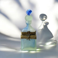 Vintage Romanian art glass perfume bottle from the 1990s, featuring frosted blue and green glass with a sculptural swirled stopper and bronze wire bow detail around the neck. Square base with a tapered neck; dauber slightly shortened due to breakage.