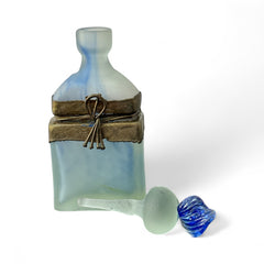 Vintage Romanian art glass perfume bottle from the 1990s, featuring frosted blue and green glass with a sculptural swirled stopper and bronze wire bow detail around the neck. Square base with a tapered neck; dauber slightly shortened due to breakage.
