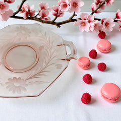 Vintage pink Depression glass serving dish with etched floral design and dual handles, styled on marble with soft lighting to highlight its shape, color, and collectible charm.