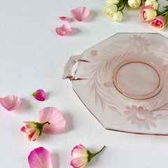 Vintage pink Depression glass serving dish with etched floral design and dual handles, styled on marble with soft lighting to highlight its shape, color, and collectible charm.