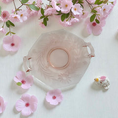 Vintage pink Depression glass serving dish with etched floral design and dual handles, styled on marble with soft lighting to highlight its shape, color, and collectible charm.